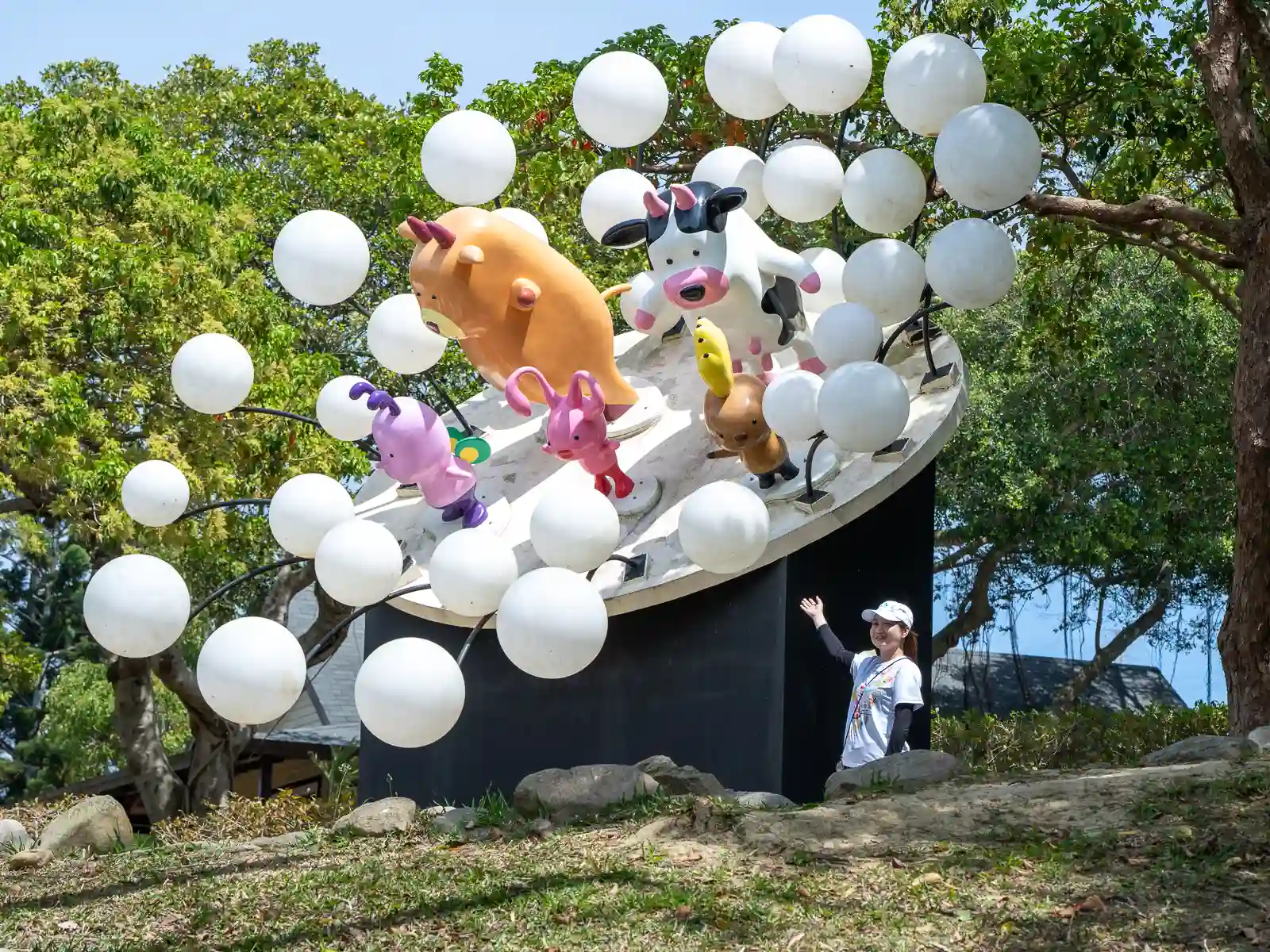 A tourist poses next to a large colorful statue of several cartoonish cows.