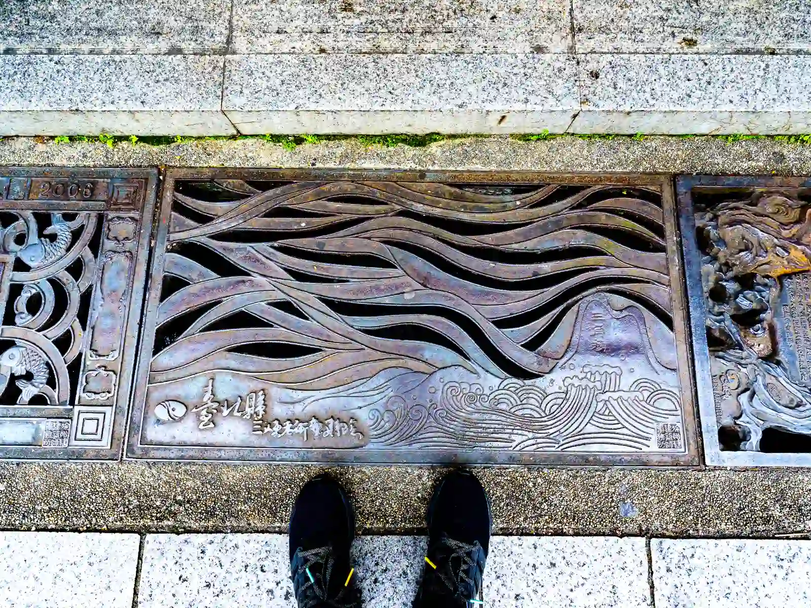 A decorative sewer grate features carved wavy patterns.