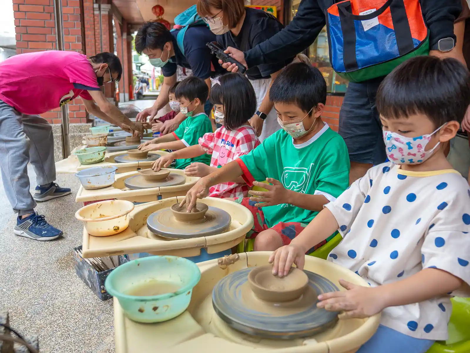 Children are using potter's wheels to shape bowls in a DIY pottery class.