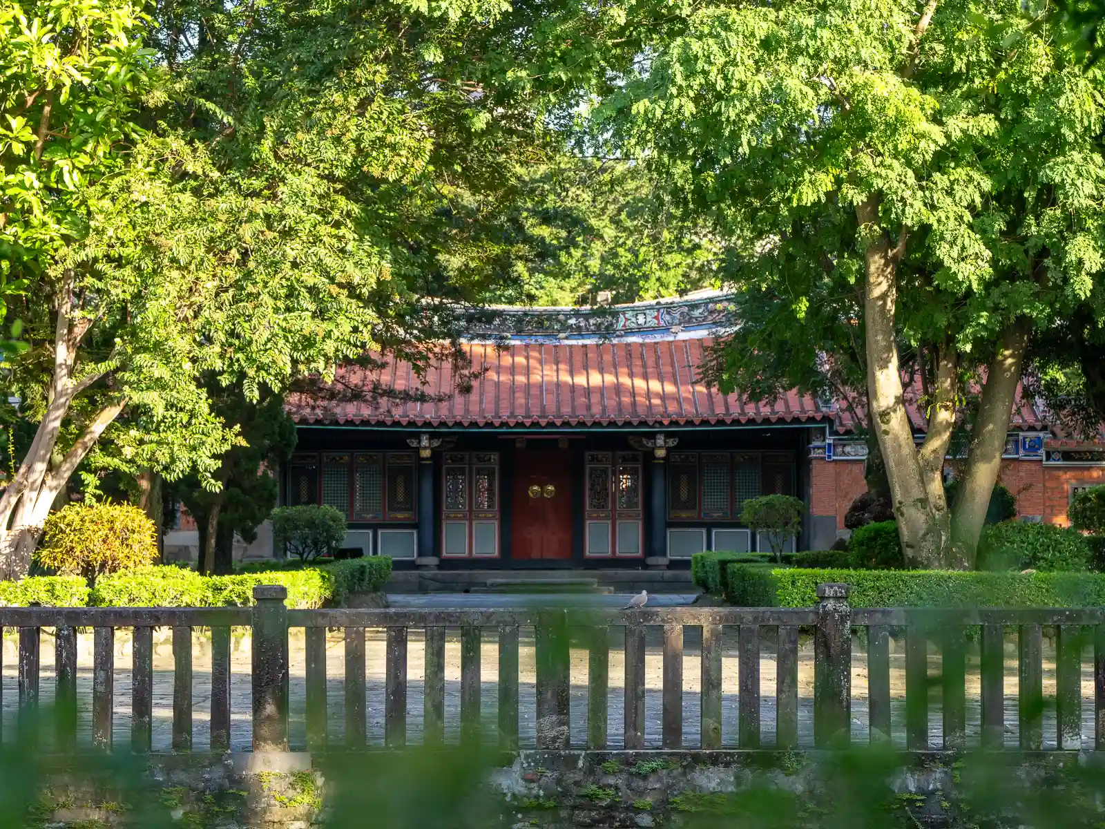 A beautifully preserved single story hall can be seen behind perfectly manicured gardens. The hall is made of red-brick and painted wood.