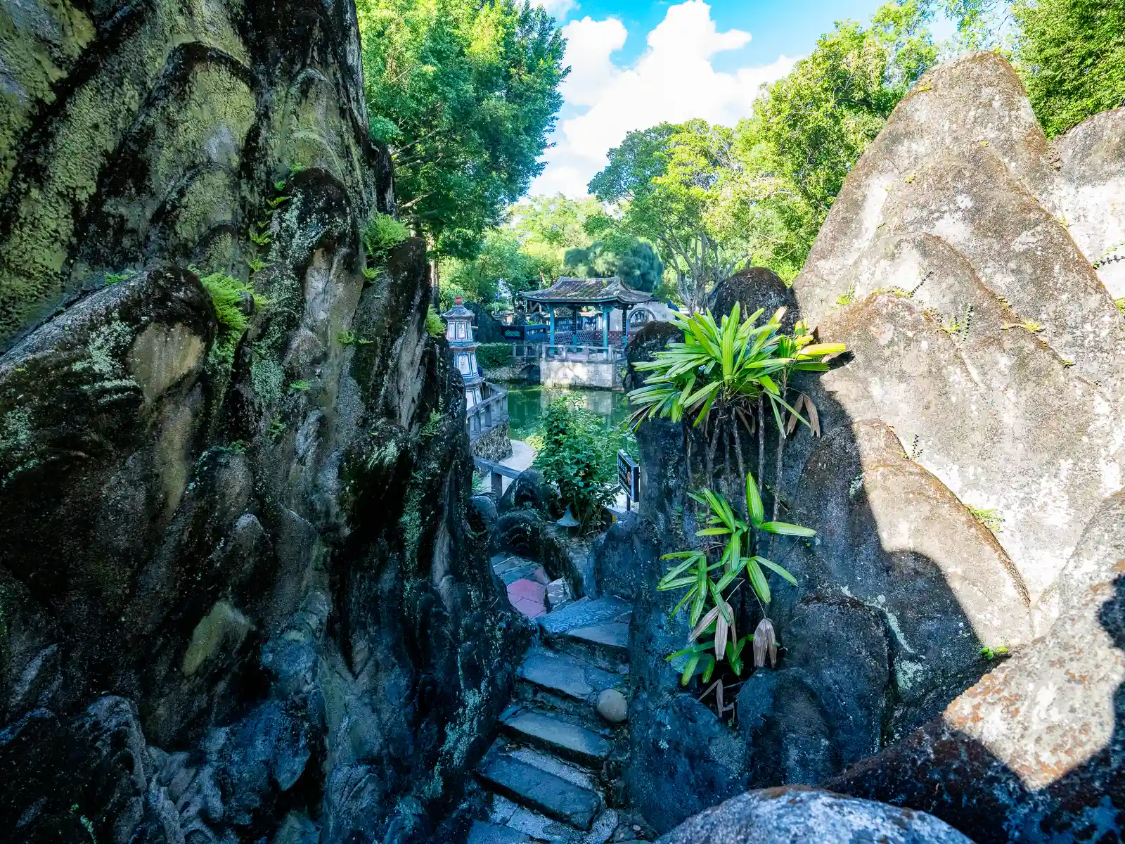 The garden path winds between several large boulders before opening up to a pond.