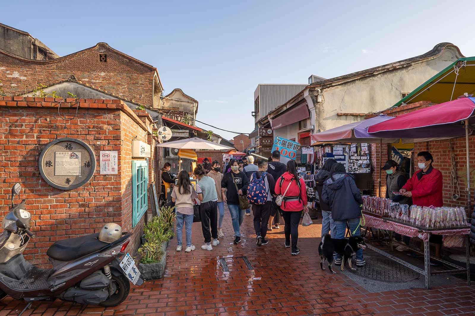Tourists walk between stalls in one of Lukang's red-brick-covered old streets; both the buildings and street are made from bright red bricks.