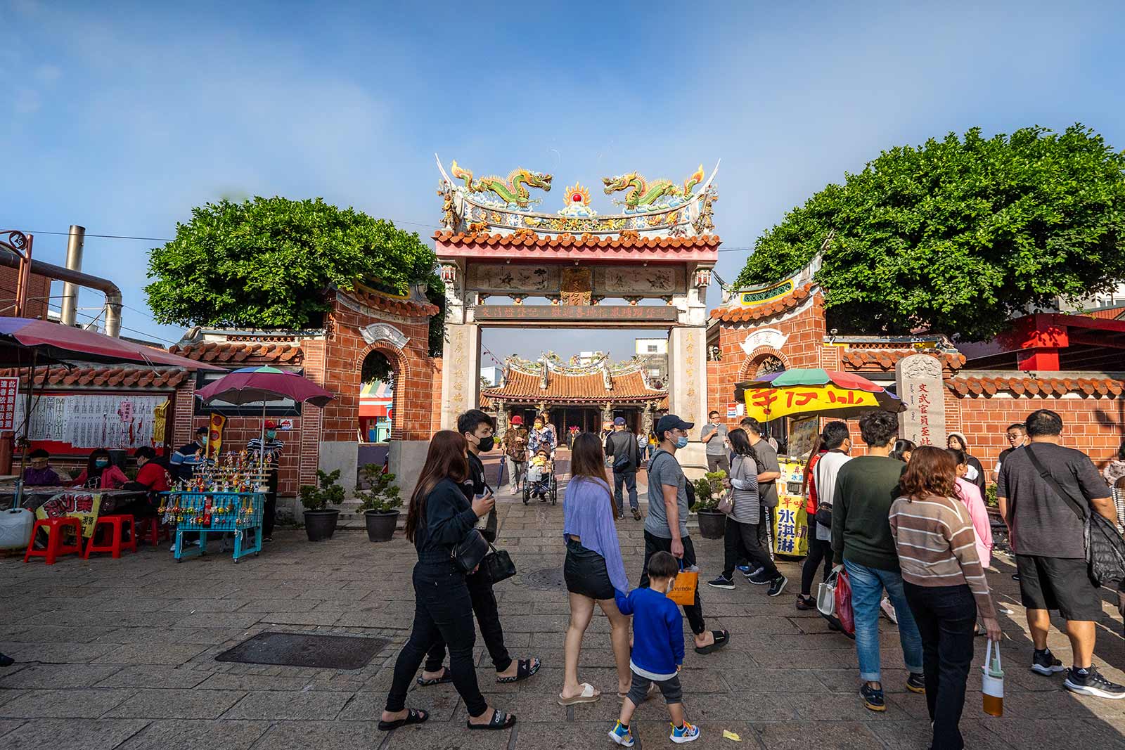 Pedestrians walk across a tile square in front of Lukang Tianhou Temple; the temple can be seen through its gate.
