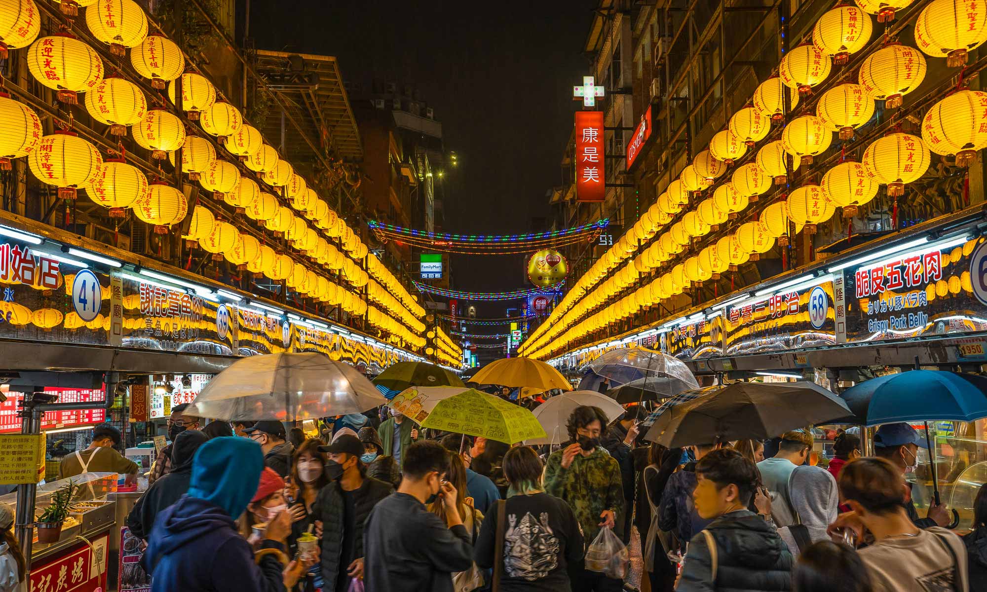 Crowds of pedestrians walking through Rensan Road at night; the road is lined by three rows of yellow lanterns on either side.