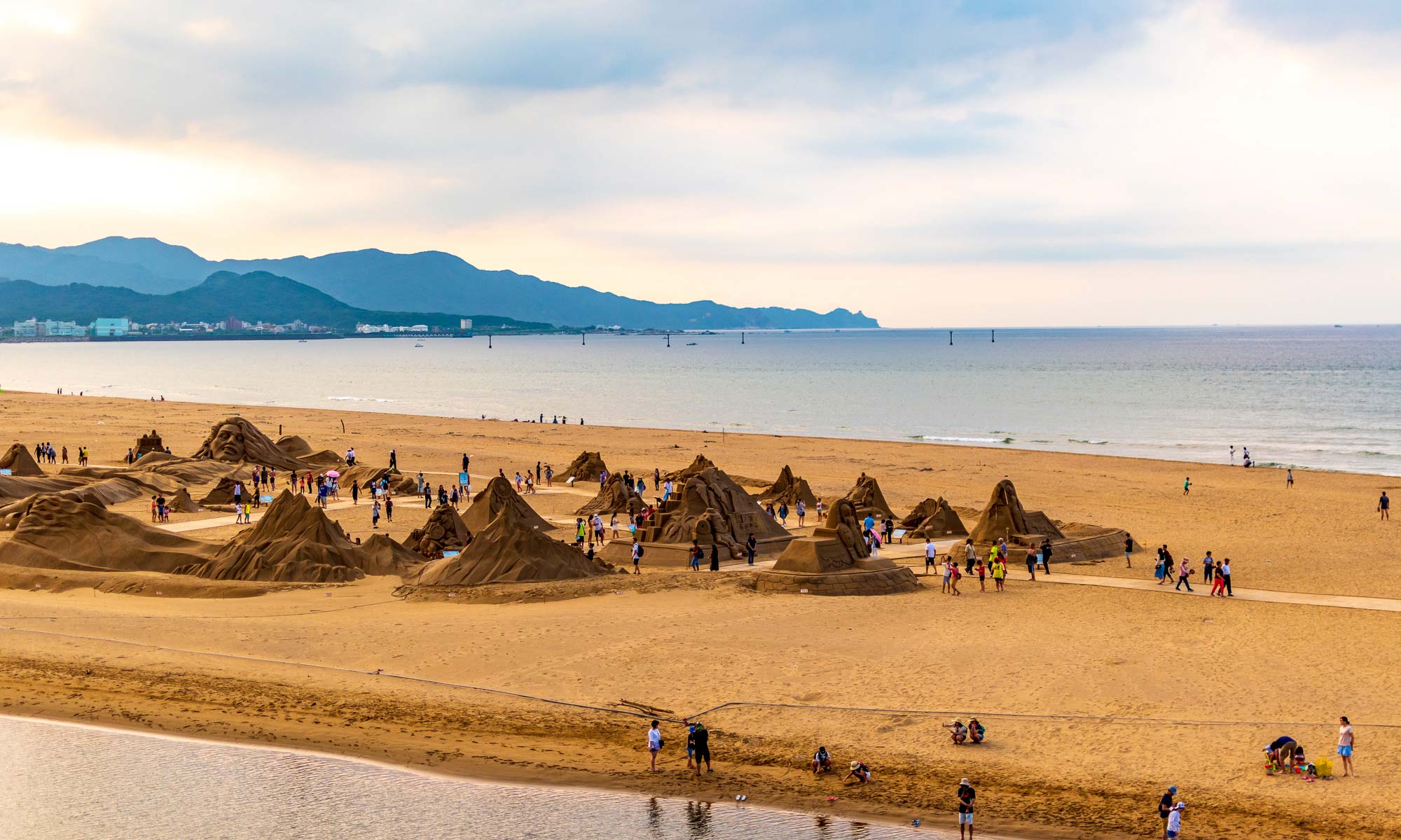 The flat and wide sandbar-like Fulong Beach is surrounded by water on both sides; the mountains of the North Coast can be seen in the background.