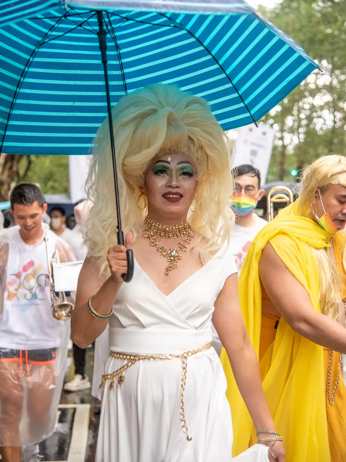 A woman in drag holds an umbrella while marching.