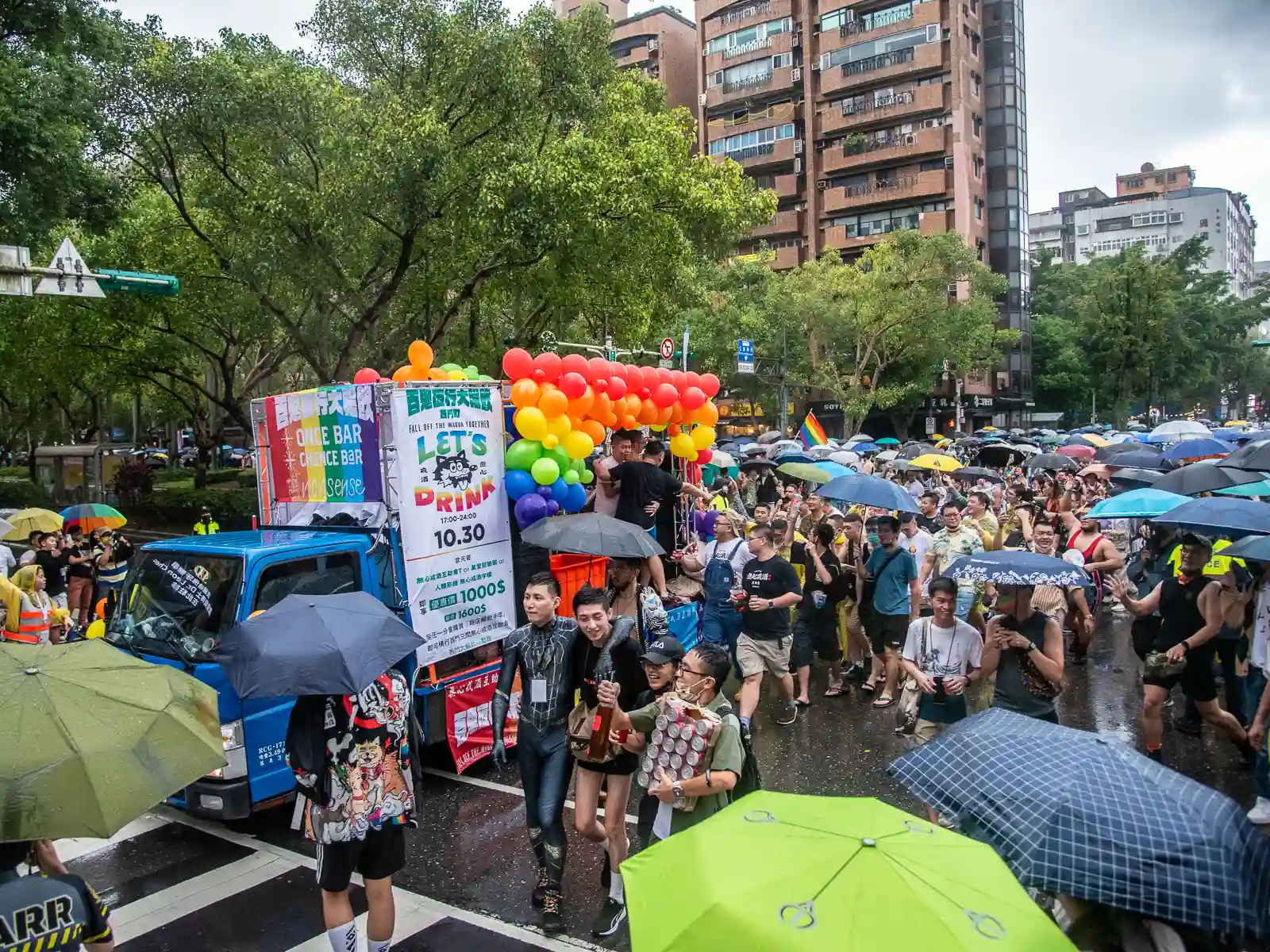A multilane intersection is completely covered by Pride Parade attendees and floats.