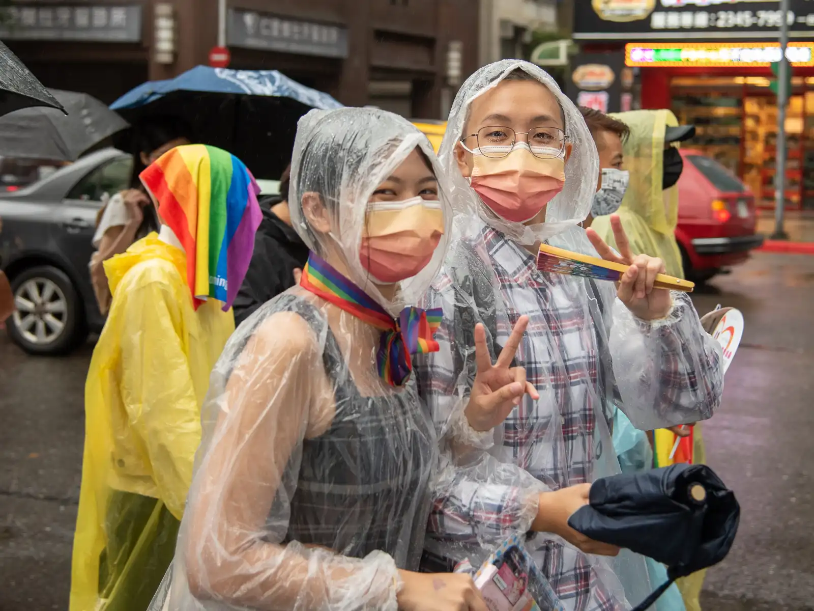Two marchers in disposable raincoats flash peace signs as the camera.