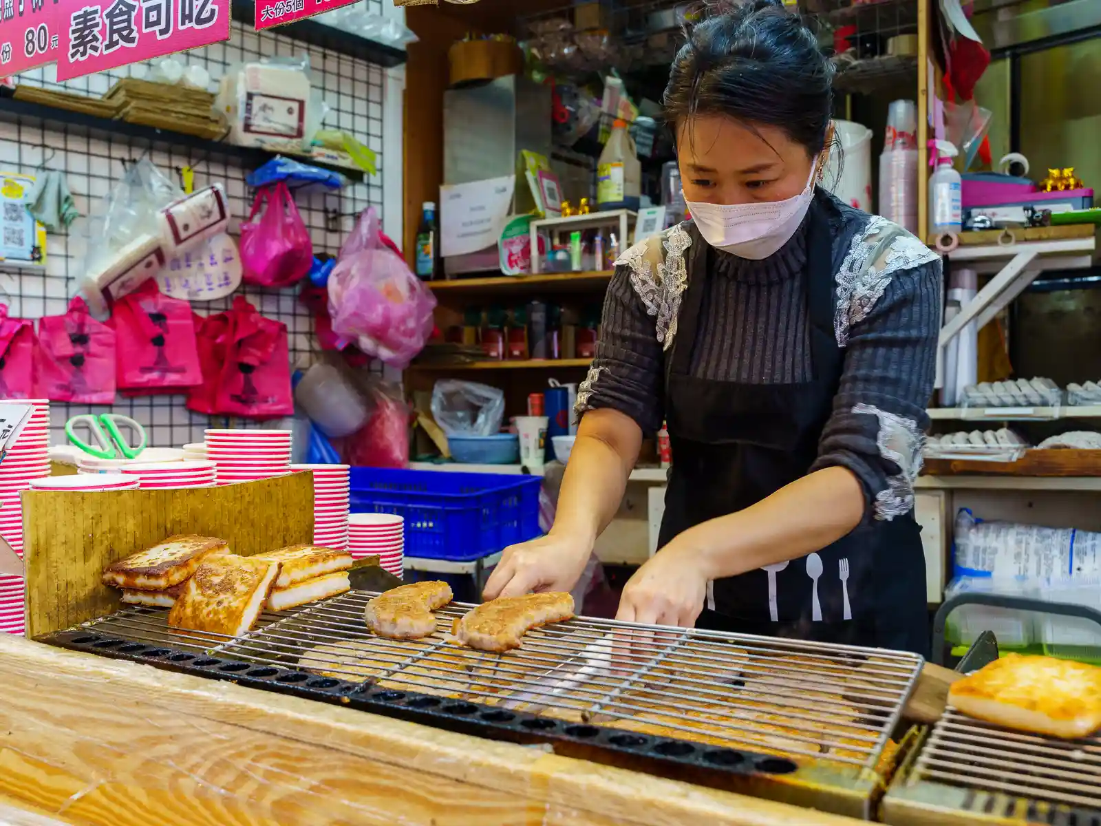 A woman is heating up taro cakes at a stand in the old street.