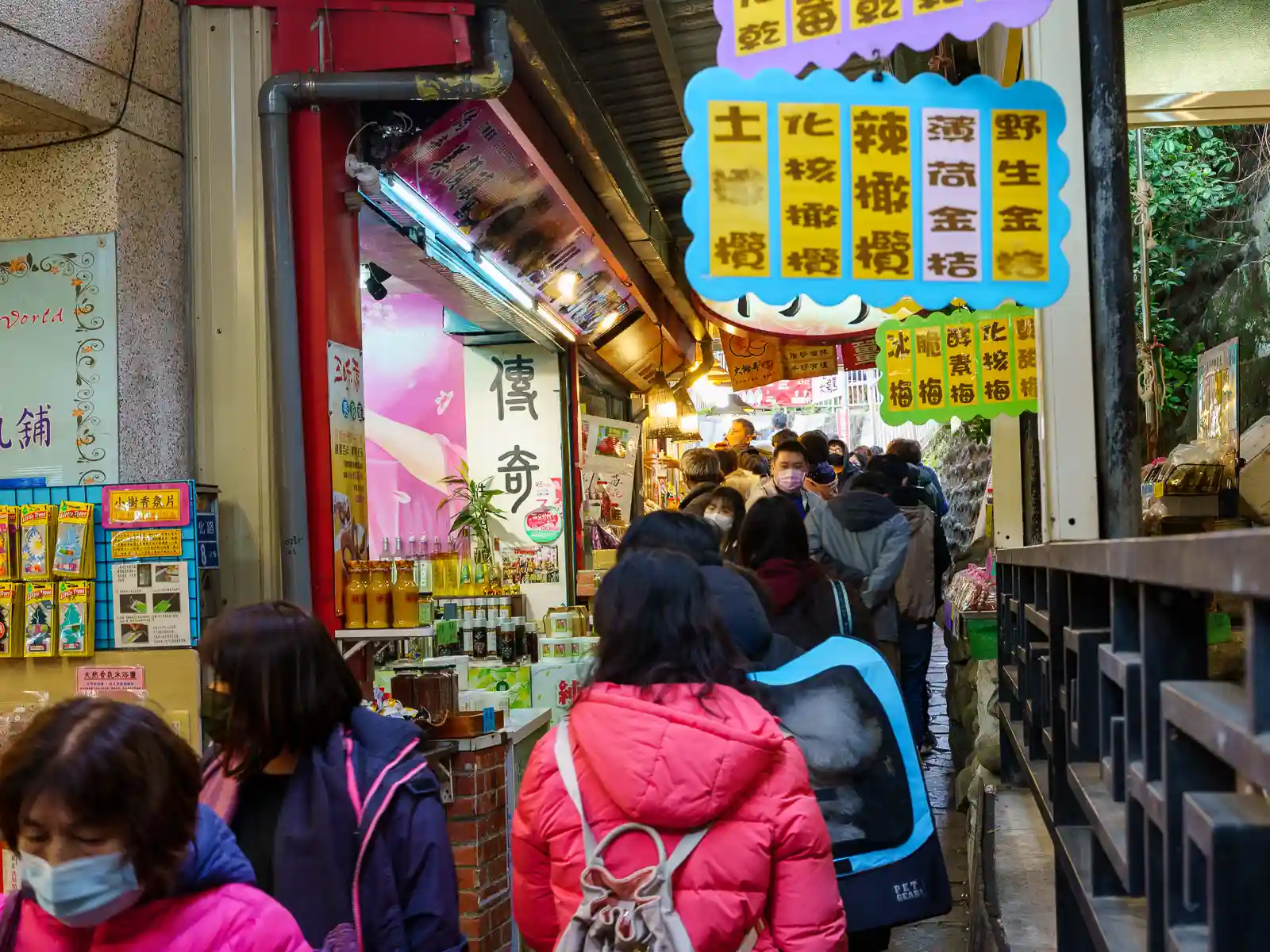 Colorful signs advertise food, snacks, and local specialties on either side of a narrow alley.