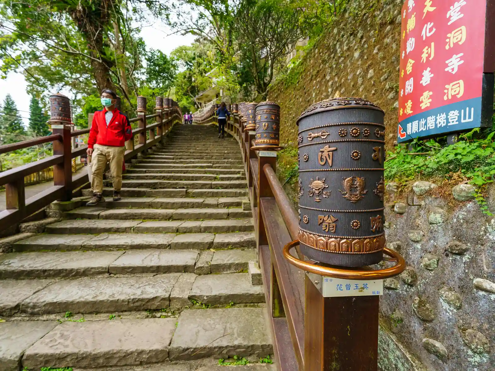 Large rotating scripture wheels adorn the railings on a wide set of stone stairs leading up the mountain.