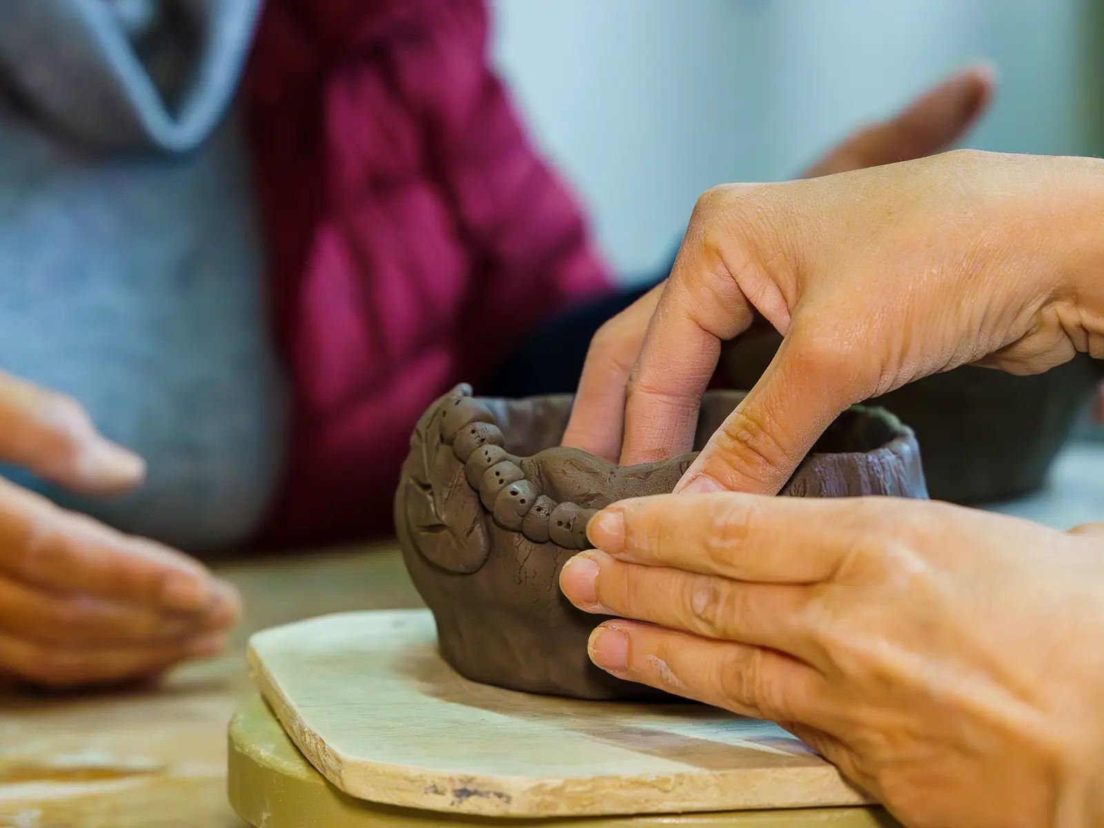 A student is using her fingers to mold a clay bowl.