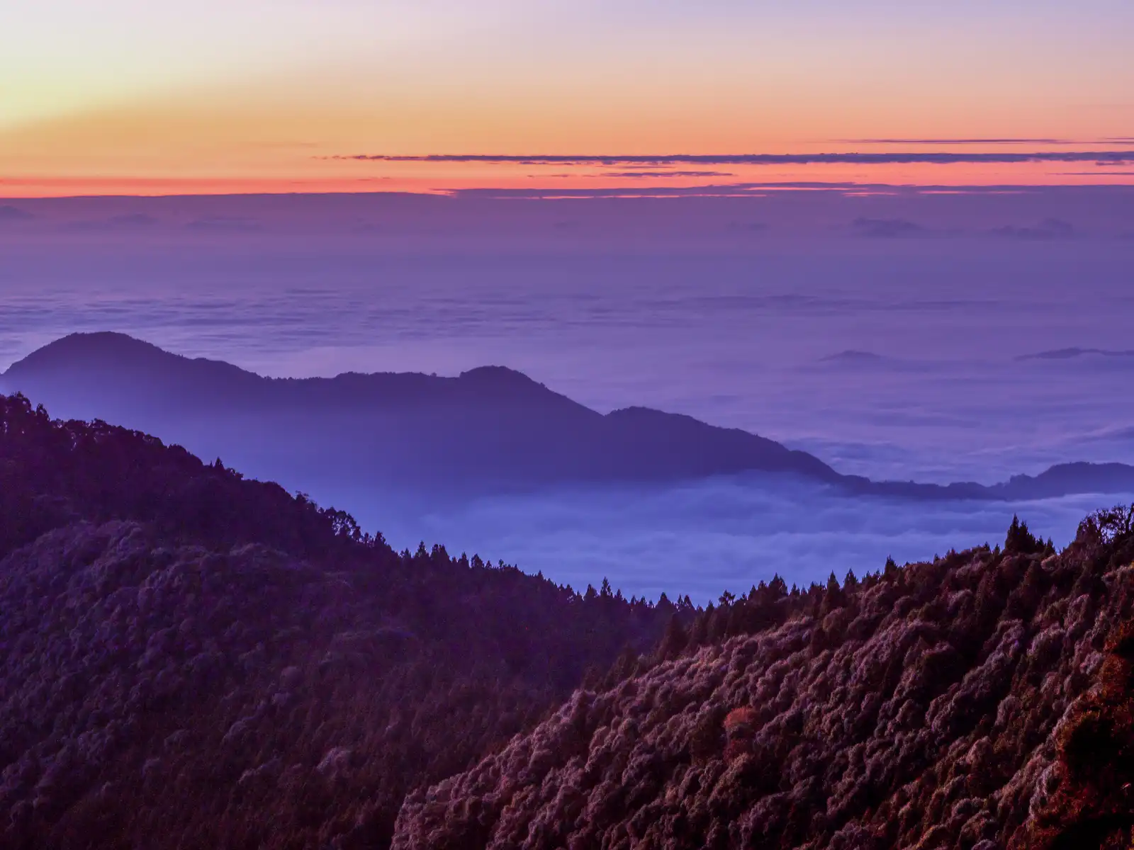 A vast sea of clouds reaches towards the horizon which is still illuminated in an orange post-sunset glow.