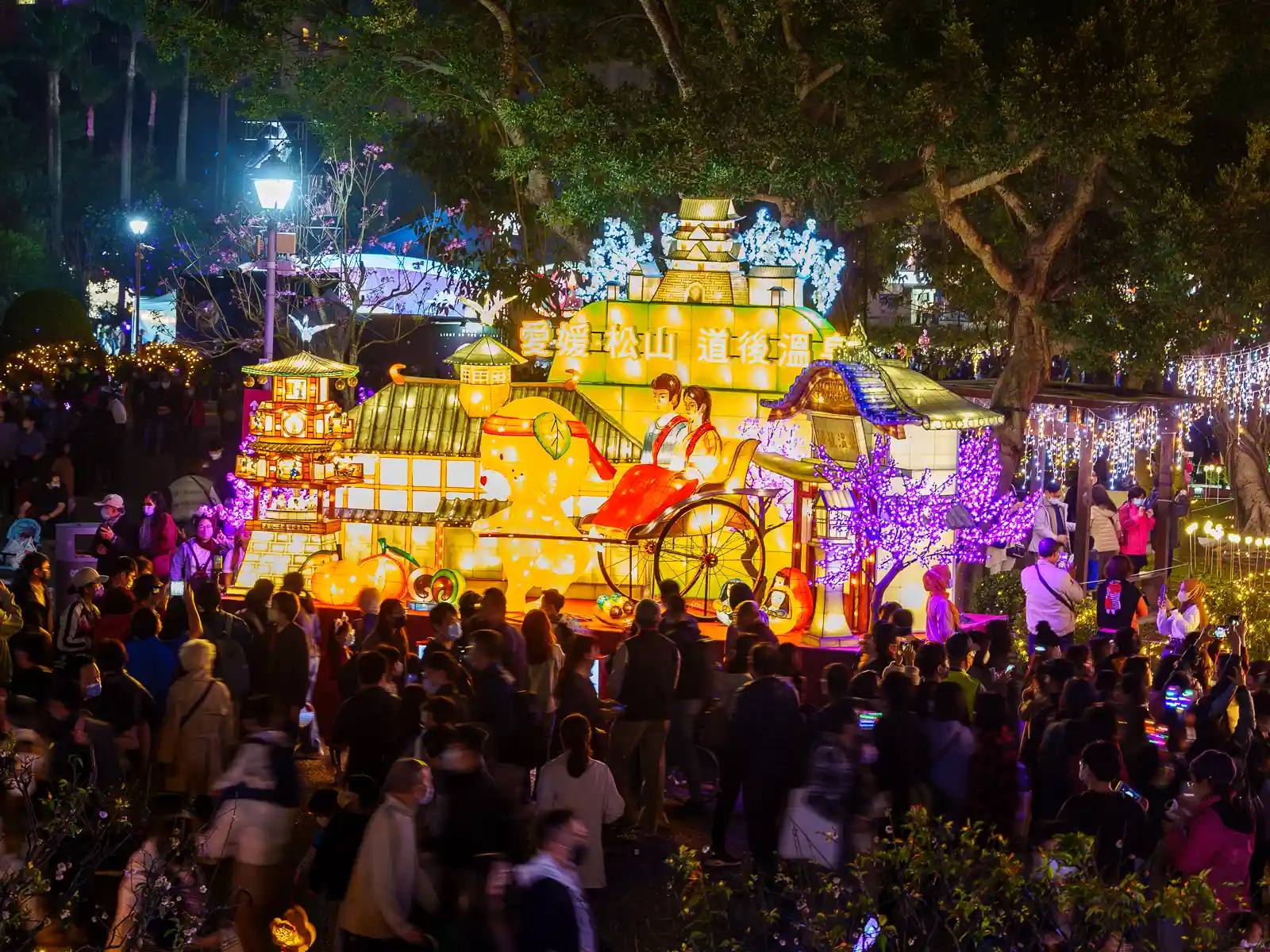 Crowds move around a lantern display which combines temples, figures, animals, and fruits.