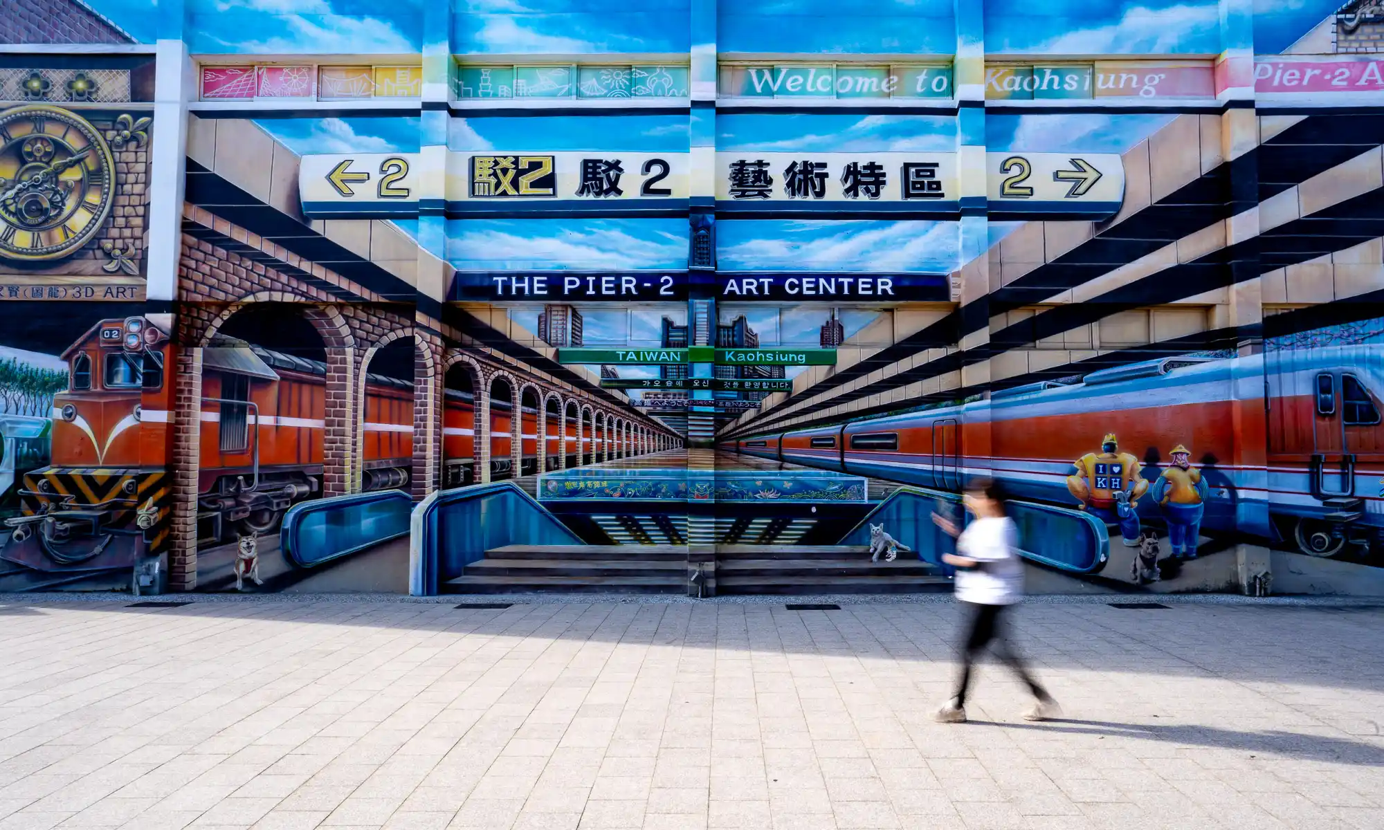 A large outdoor mural of a train station can be seen on the side of a warehouse.