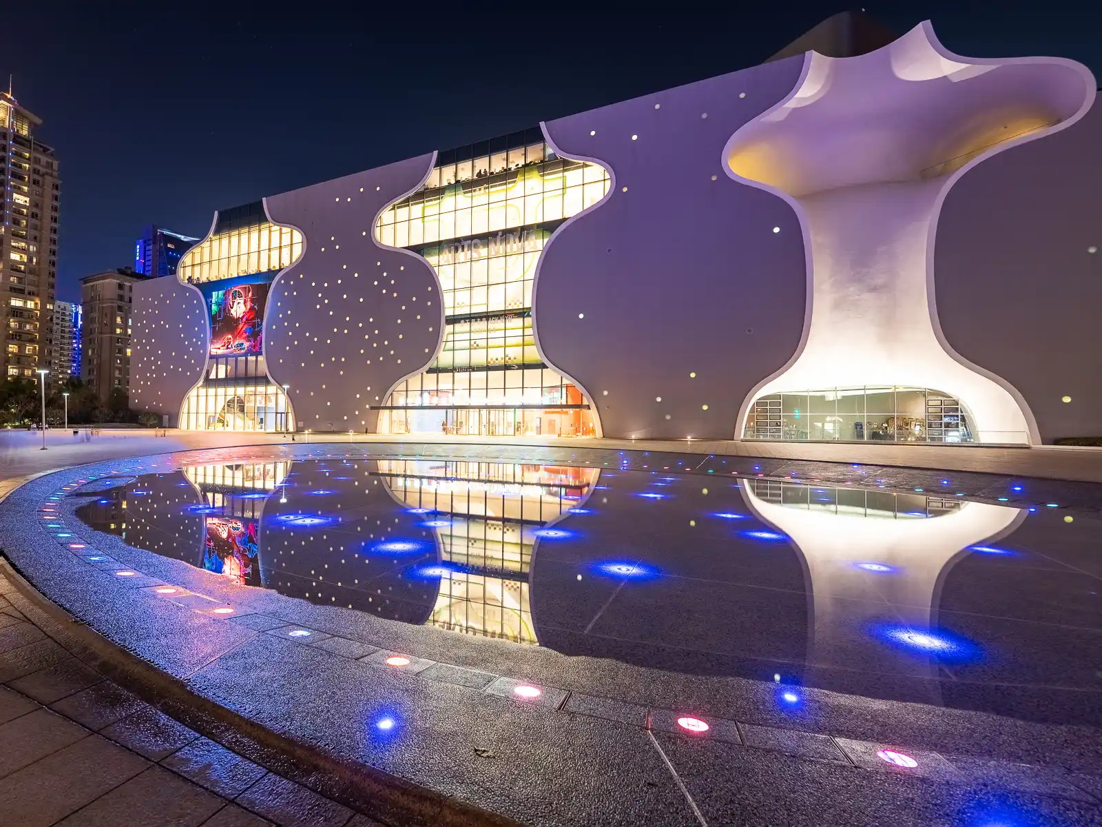 The outdoor fountain and theater are elegantly illuminated at night.
