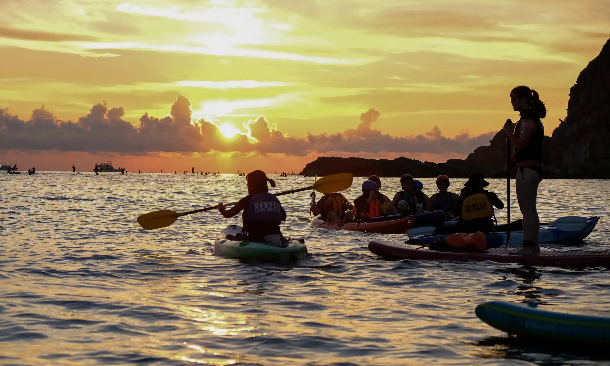 A group of kayakers and paddlers view the sunrise from the ocean.