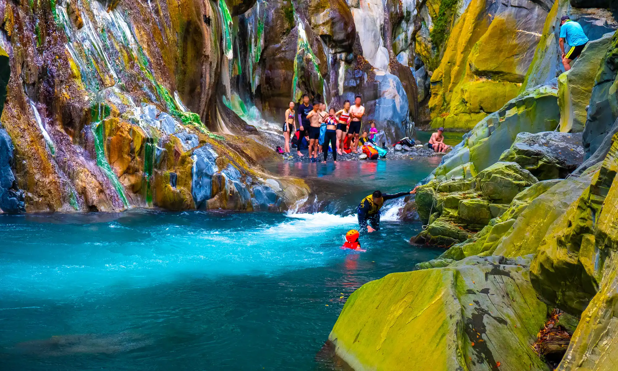 A crowd looks on as a guide helps a child cross a pool on the way to Lisong Hot Spring.