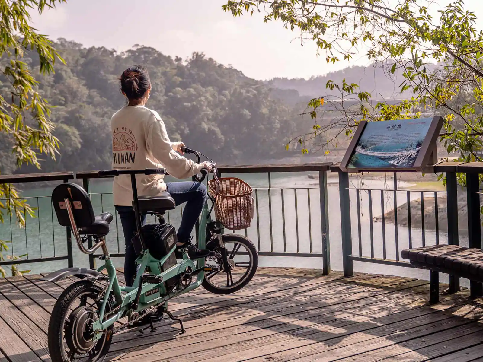 A tourist with a tandem bicycle rests at an overlook and takes in the landscape of a lake.