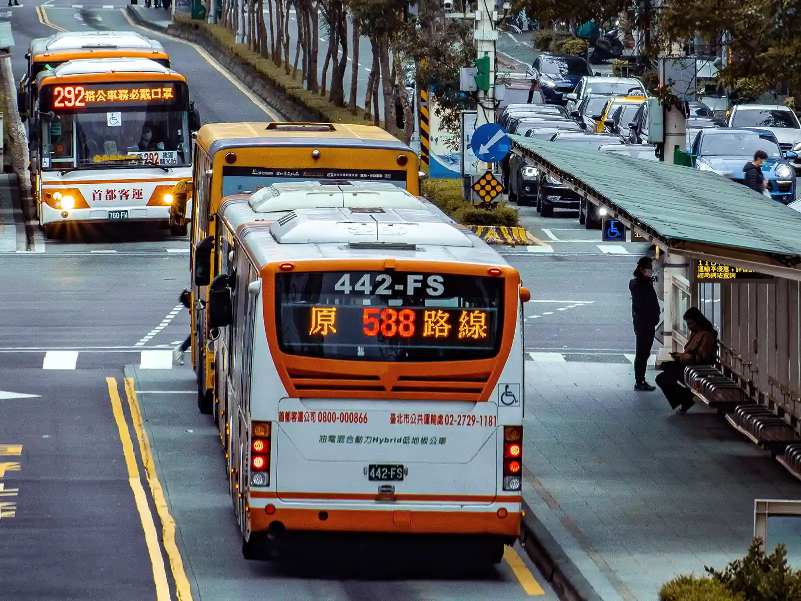 Several busses are stopped at a bus station located in the middle of a road.