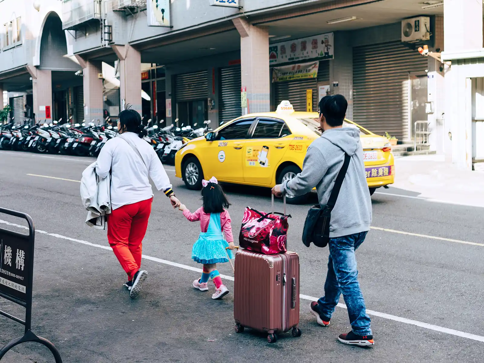 A family with luggage walks by a taxi cab.