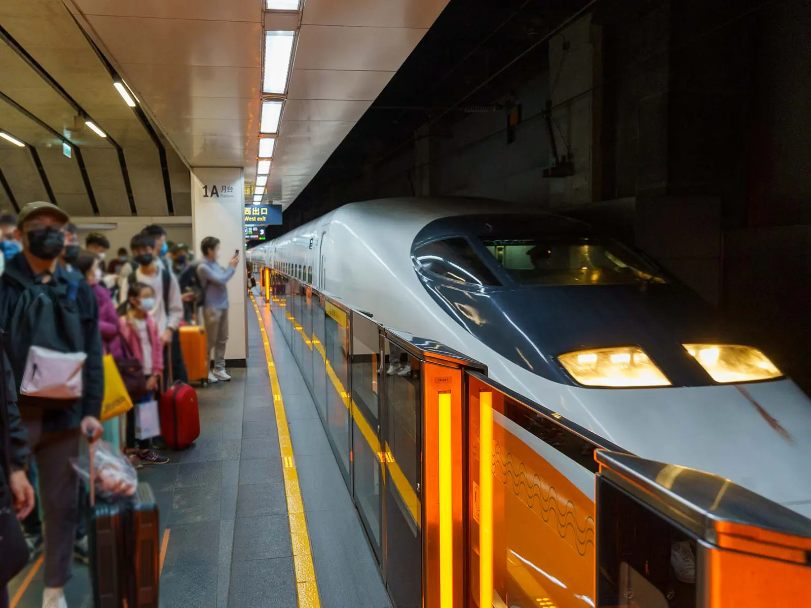 Passengers waiting on a platform as a high-speed train with sleek design arrives at the station.