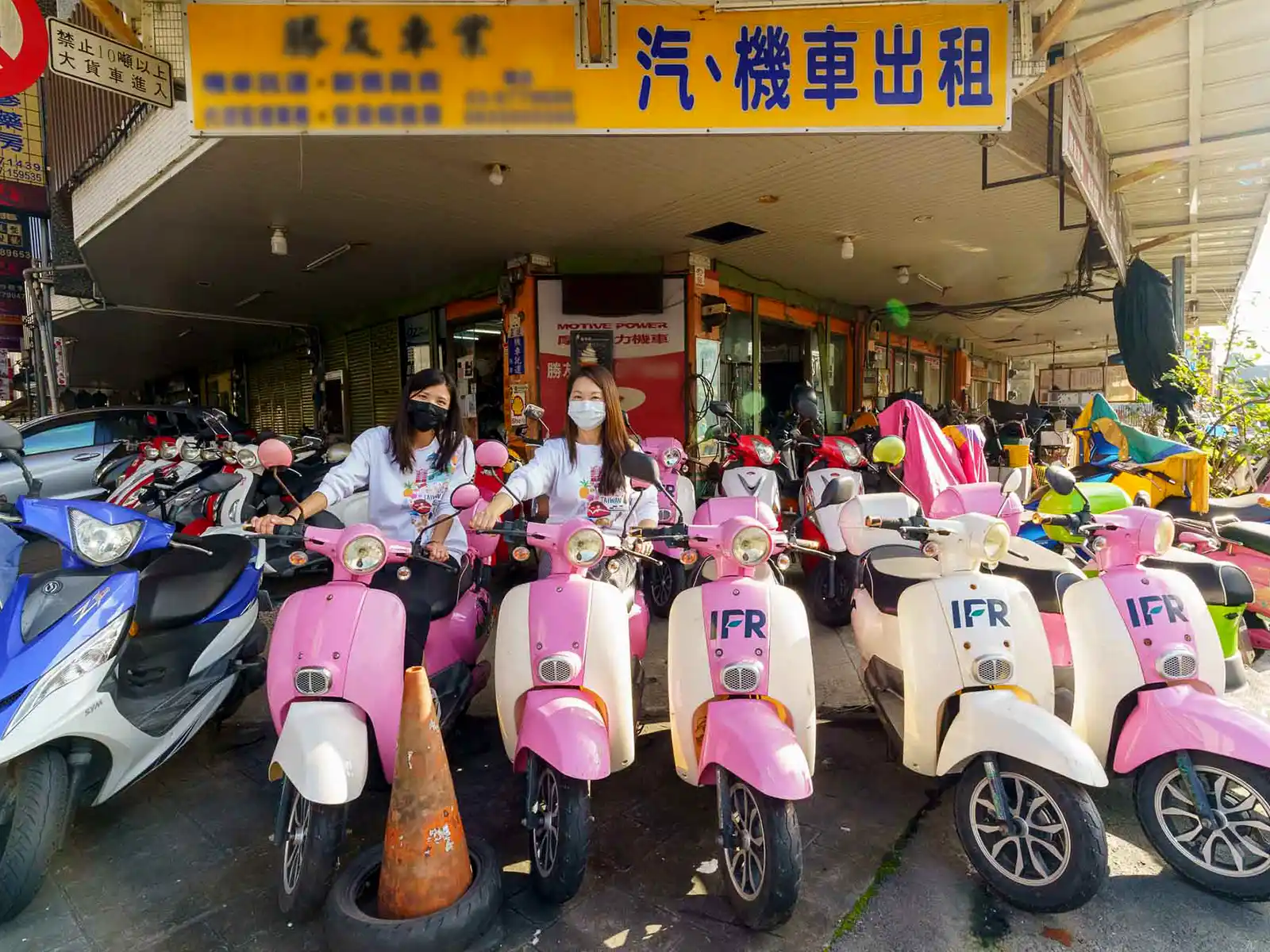 A busy scooter rental shop with a row of pink and other colorful scooters lined up in front.
