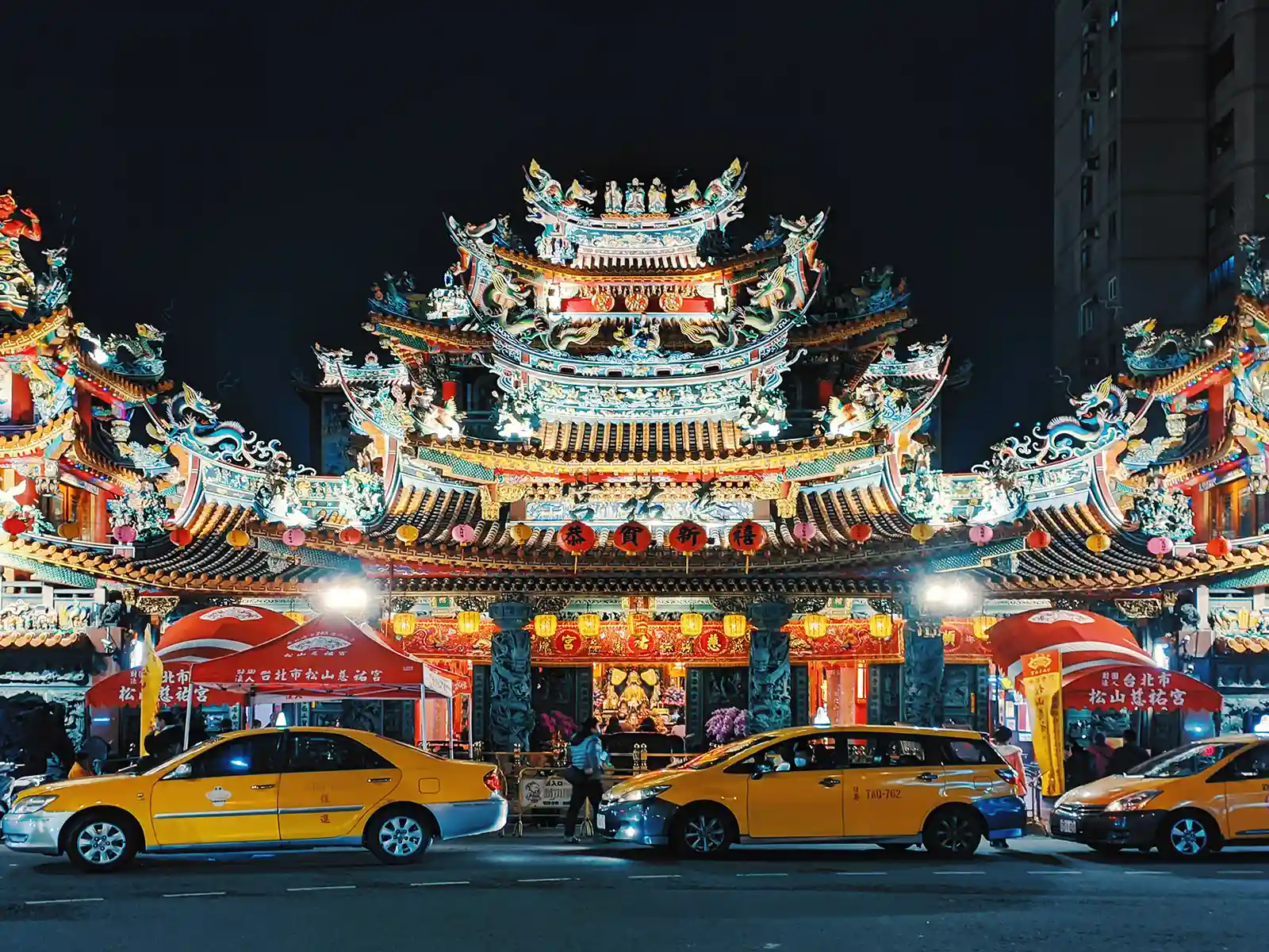Several taxis are parked in front of an ornately decorated temple.
