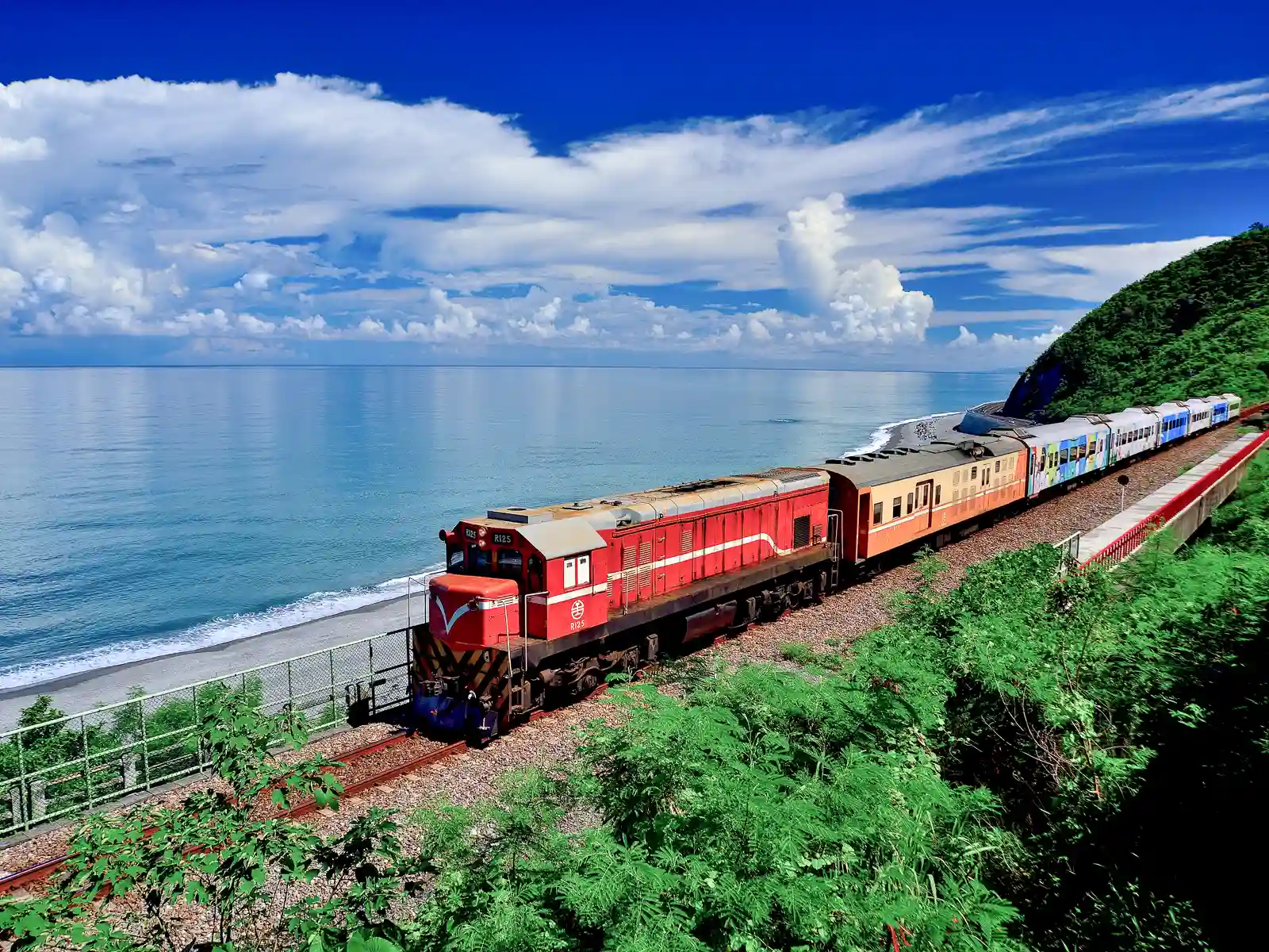 A colorful train traveling in front of the Pacific Ocean.